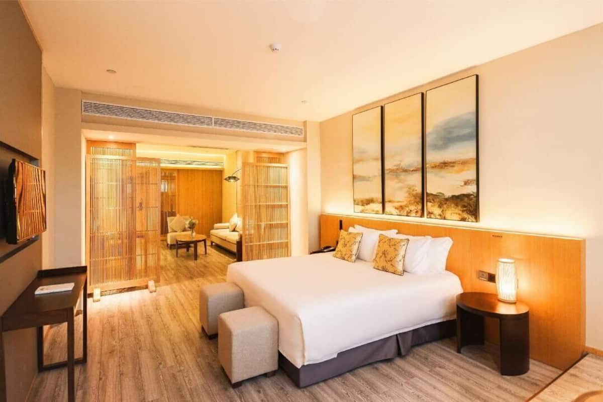 A hotel room with a large bed, a bedside table, a nightstand, a wall-mounted TV, and a large window.