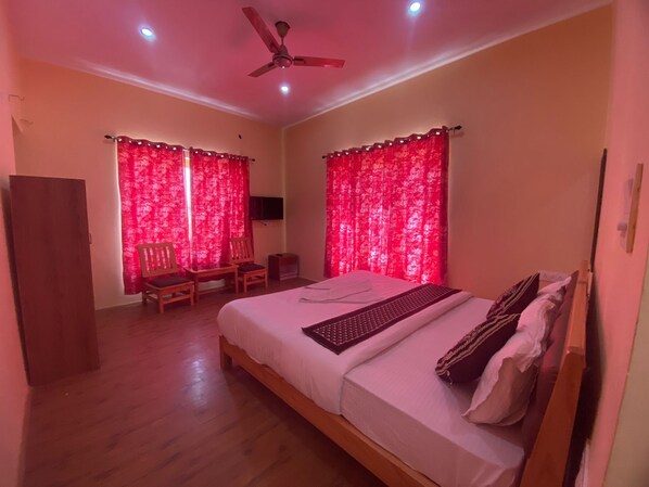 A bedroom with a bed, two chairs, a ceiling fan, and red curtains.