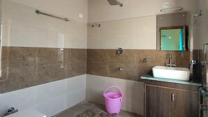 A bathroom with a toilet, sink, shower, and a pink bucket on the floor. - LUNGDHO RESIDENCY (Leh)