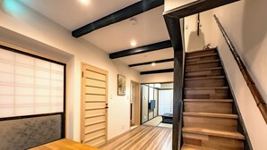 A modern interior with a wooden staircase, a large wooden table, and traditional sliding doors.