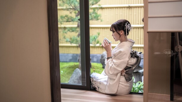 A person sitting by a window with a view of a garden.