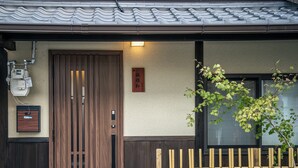 A traditional Japanese building with a wooden door, a bamboo fence, and a sign on the wall.