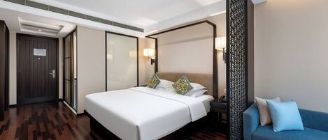 A modern hotel room with a large bed, a blue sofa, and a decorative partition.