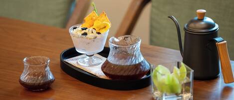A tray with a dessert, a glass of beverage, a small pitcher, and a coffee pot on a wooden table.
