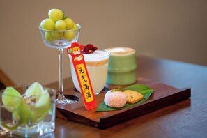 A table with a glass bowl of green apples, a glass of white beverage, a green container, and a wooden tray with a small cake and a decorative item. - SSAW Boutique Hotel Hangzhou East Railway Station - Close to West Lake (Hangzhou)
