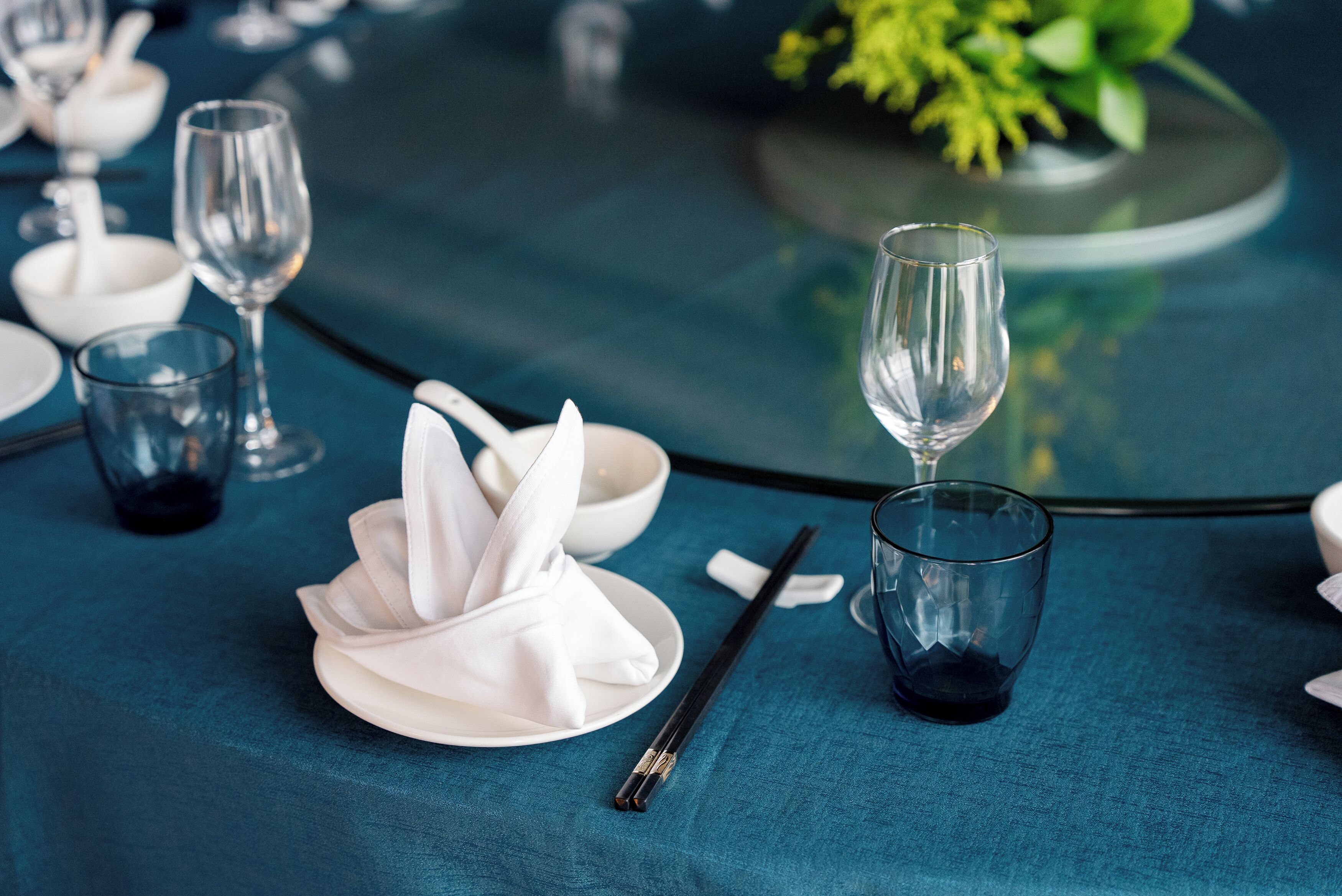 Une table dressée avec des assiettes, des verres et des baguettes sur une nappe bleue.