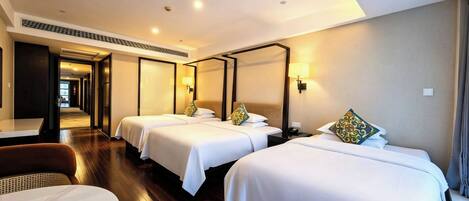 A hotel room with three beds, a dining table, and a view of the hallway.