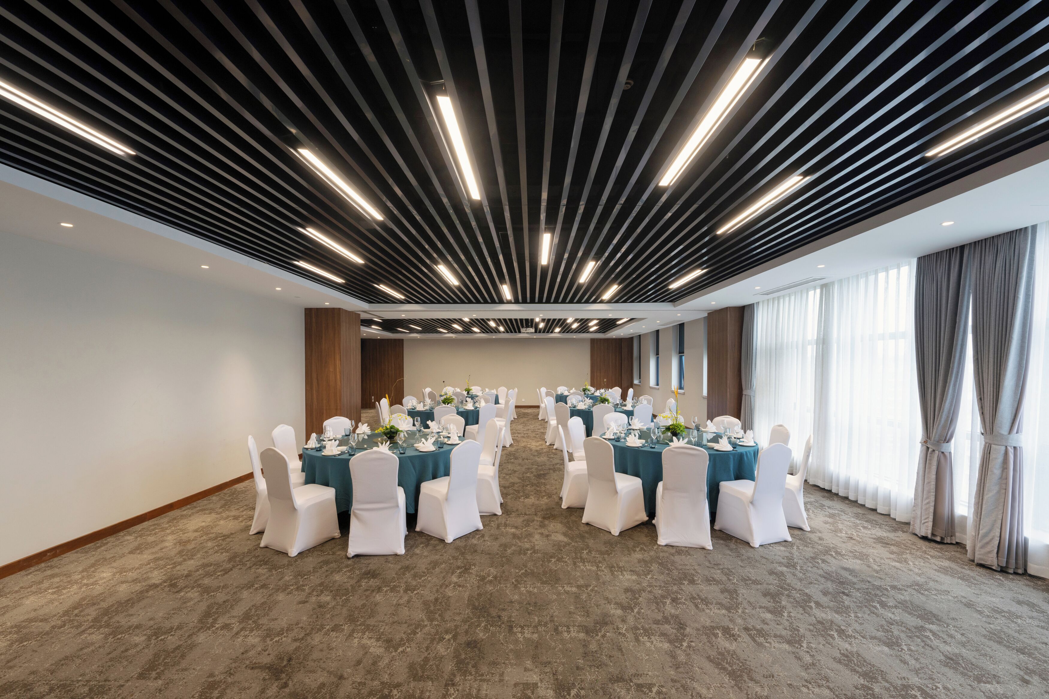 Un salón de conferencias con filas de mesas, sillas blancas y un diseño moderno del techo.