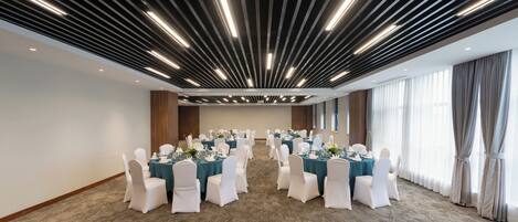 Un salón de conferencias con filas de mesas, sillas blancas y un diseño moderno del techo.
