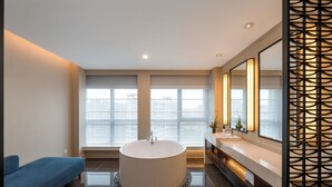 Ein modernes Badezimmer mit einer freistehenden Badewanne, einem Waschtisch mit Spiegel und einem großen Fenster mit Blick auf die Stadt.