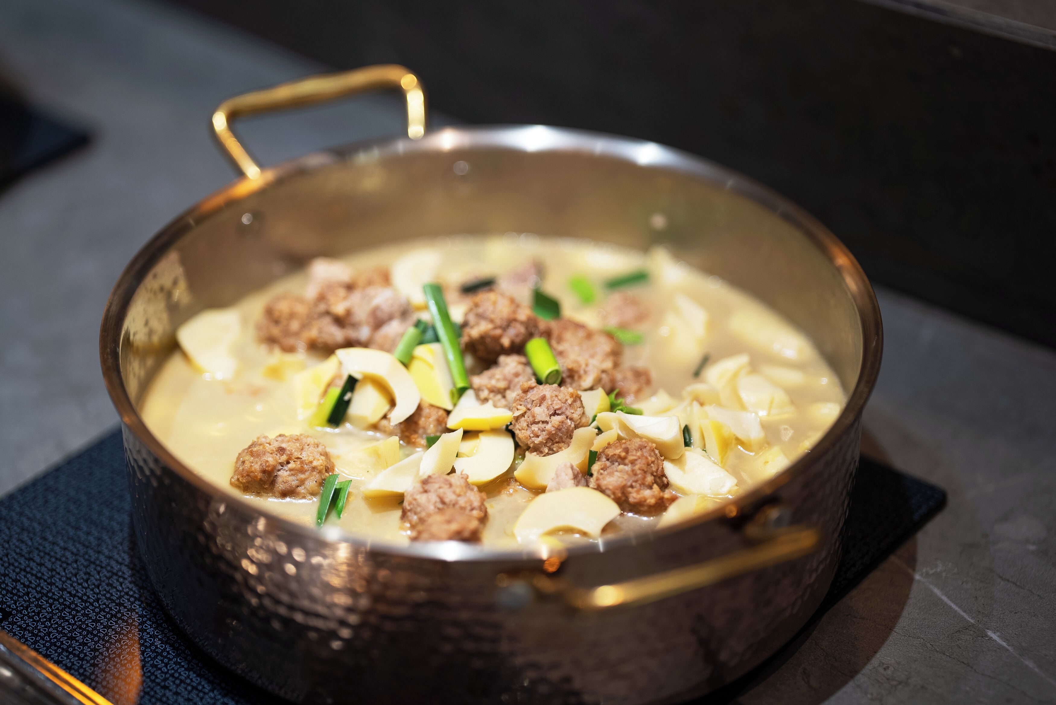 A pan of soup with meatballs and vegetables.