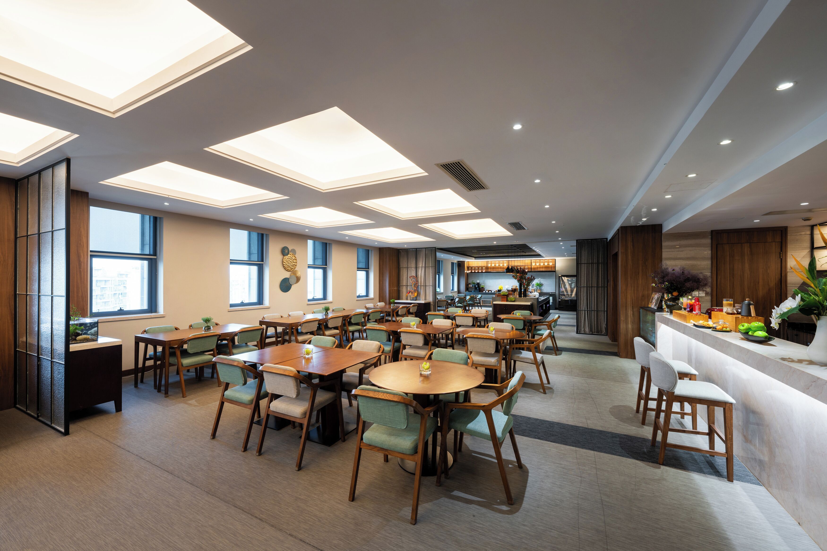 A spacious dining area with multiple tables and chairs, a bar counter, and large windows allowing natural light.