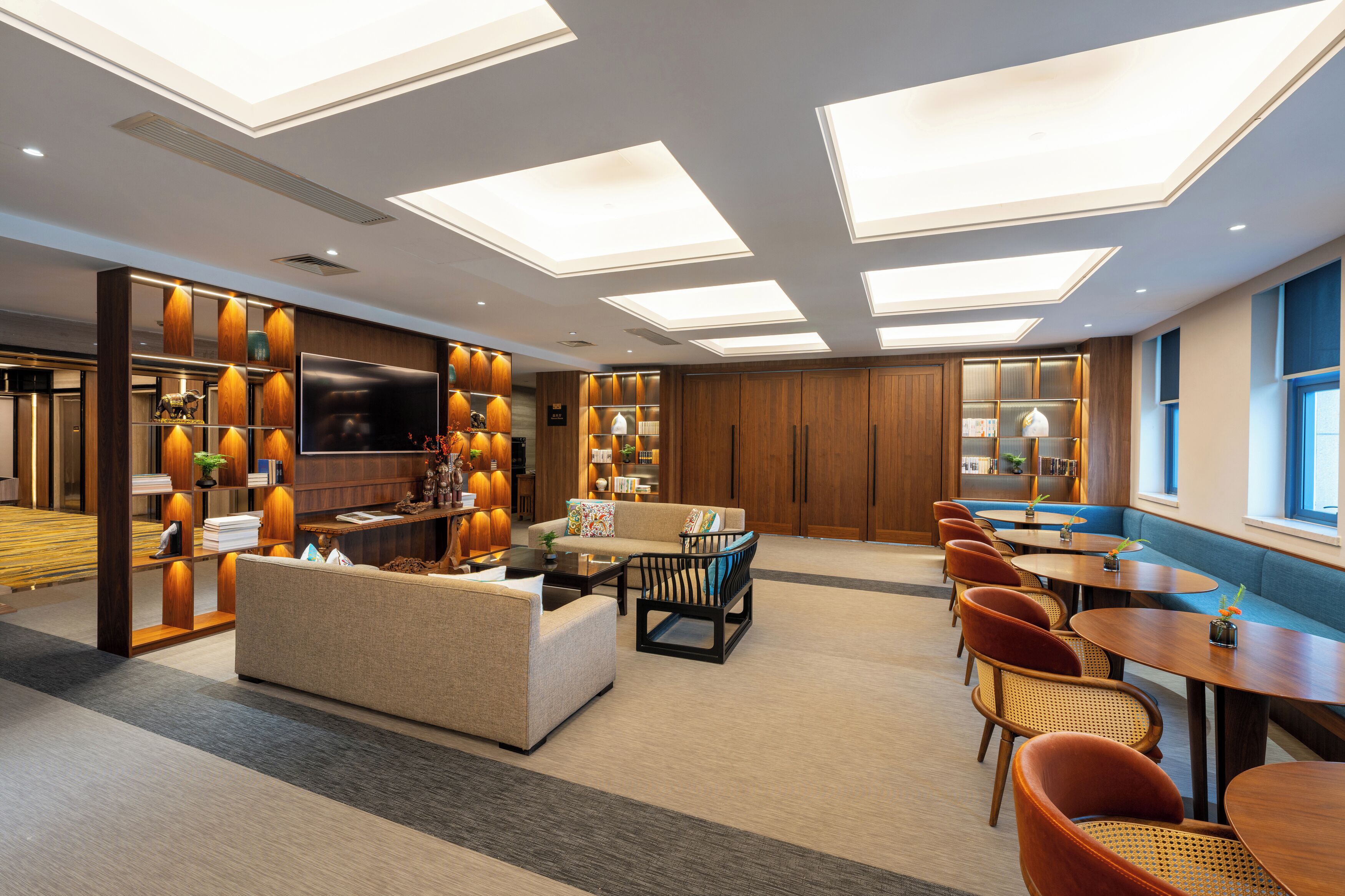 Un hall d’hôtel moderne avec un canapé, une table basse et un coin salon, comprenant un téléviseur à écran plat, des meubles en bois et une grande fenêtre.