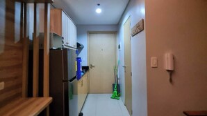 Un pasillo estrecho con un banco de madera a la izquierda, un refrigerador y una mopa a la derecha.