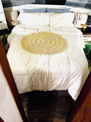 Una cama con edredón blanco y una manta circular tejida.