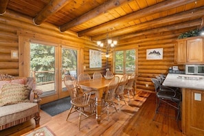 L’intérieur d’une cabane en rondins comprend une table à manger, des chaises, un canapé, un coin cuisine et de grandes fenêtres.