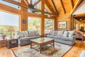 A log cabin interior with a large window, a sofa, a coffee table, and a rug.