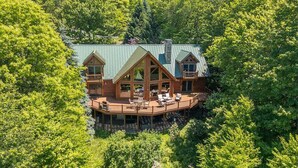 A cabin with a deck, surrounded by dense forest. - Deep Creek Escape | Fireplace + Hot Tub (McHenry)