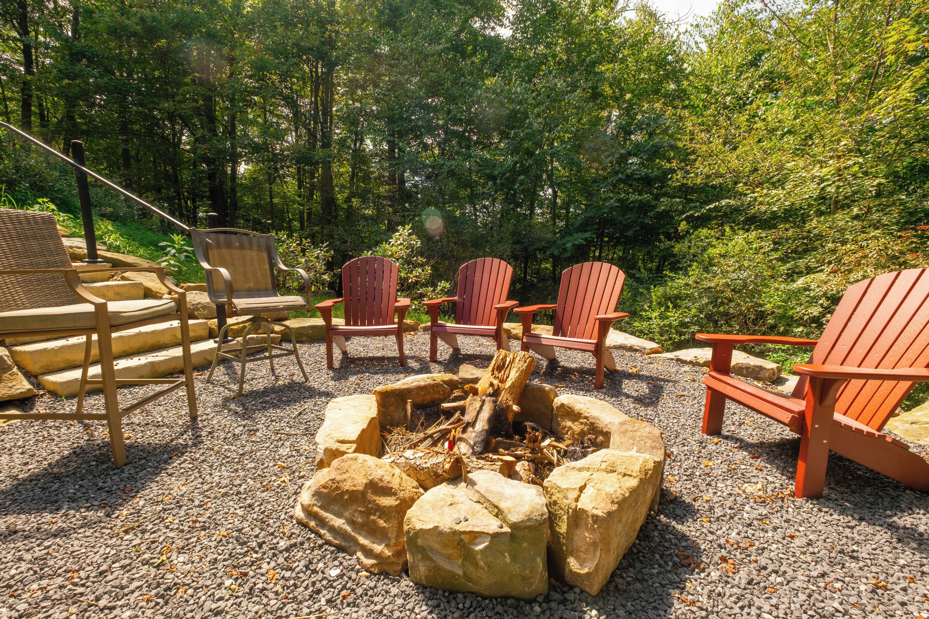 Una chimenea rodeada de sillas Adirondack en un área boscosa.