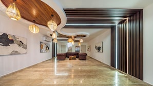 Un amplio pasillo con piso de mármol pulido, sofá de cuero y techo de madera con luces colgantes.