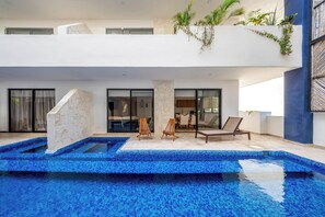 Een modern zwembadterras met een stenen constructie, ligbedden en een glazen eethoek.