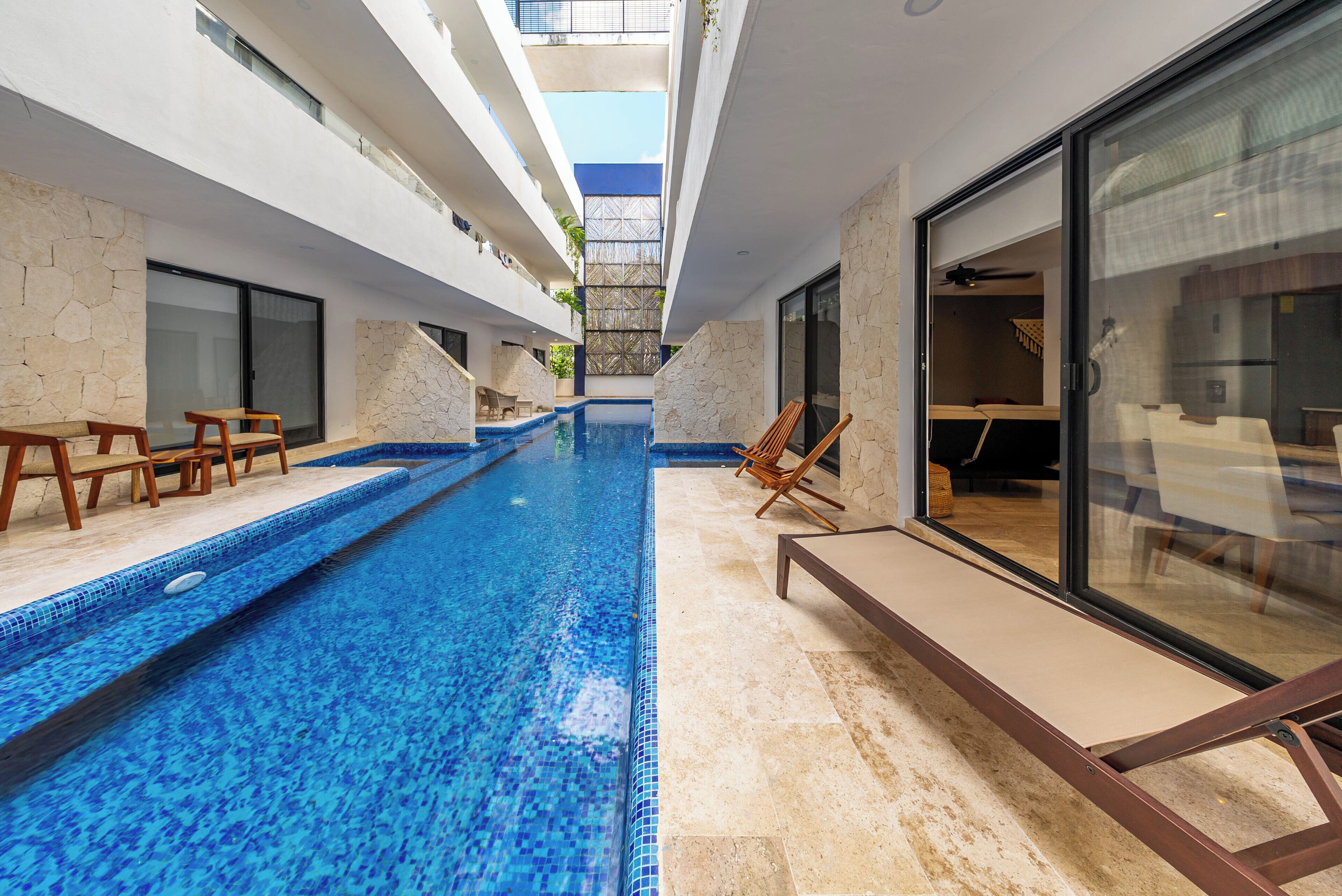 Une piscine intérieure moderne, avec une eau d’un bleu limpide, des murs en pierre et des chaises longues en bois.
