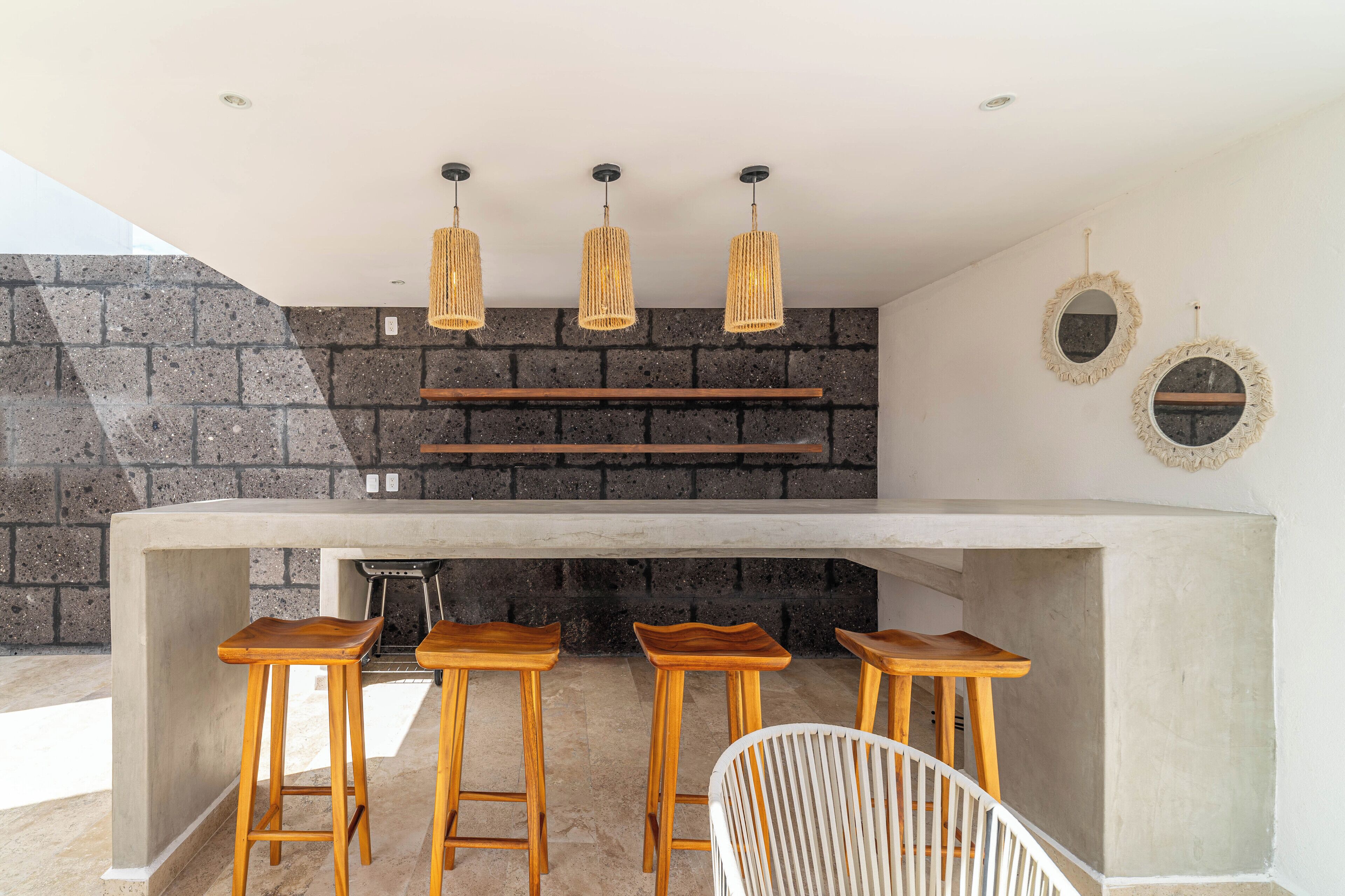 Une cuisine avec un mur en pierre, des tabourets en bois, une chaise blanche et des luminaires suspendus.