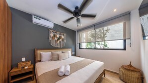 Un dormitorio moderno con una cama grande, ventilador de techo, ventana con vistas y aire acondicionado de pared.