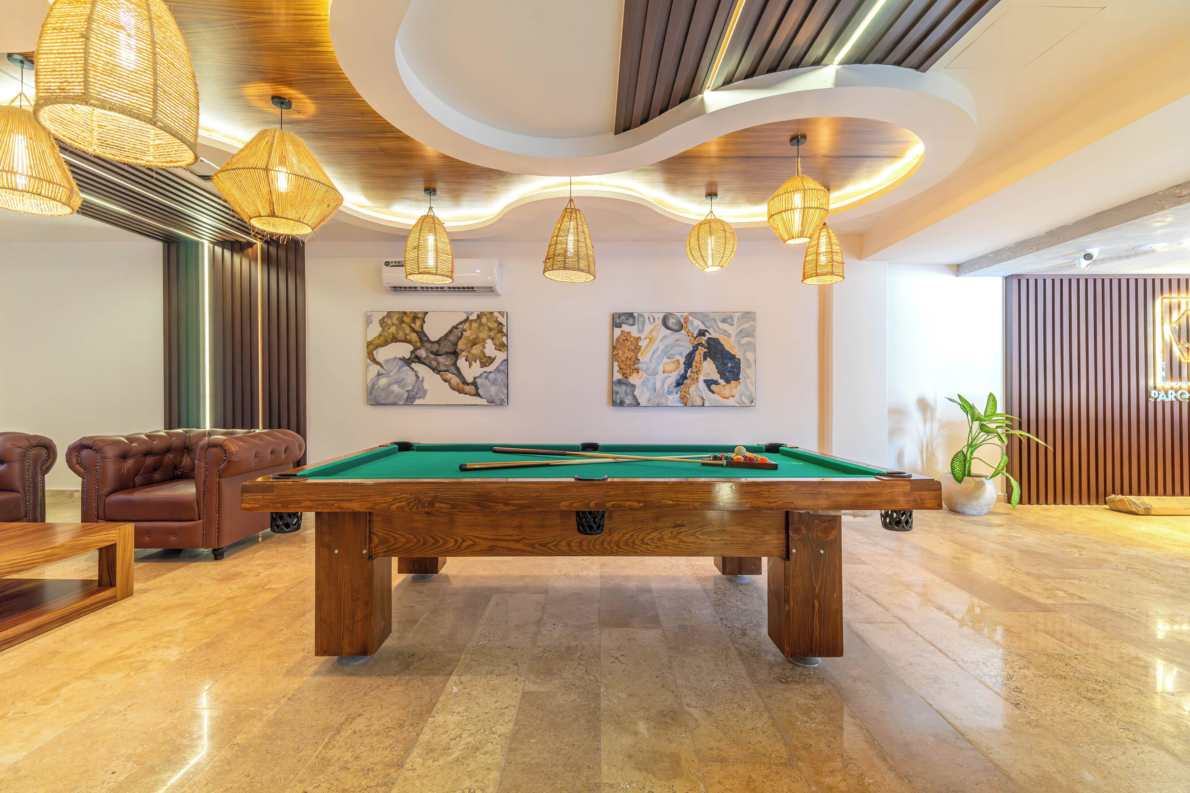 Une table de billard dans une pièce bien éclairée, décorée dans un style moderne, avec notamment un canapé et des œuvres d’art accrochées aux murs.
