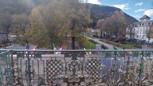 A balcony with ornate metal railings overlooking a town with autumn-colored trees and a mountain in the background.