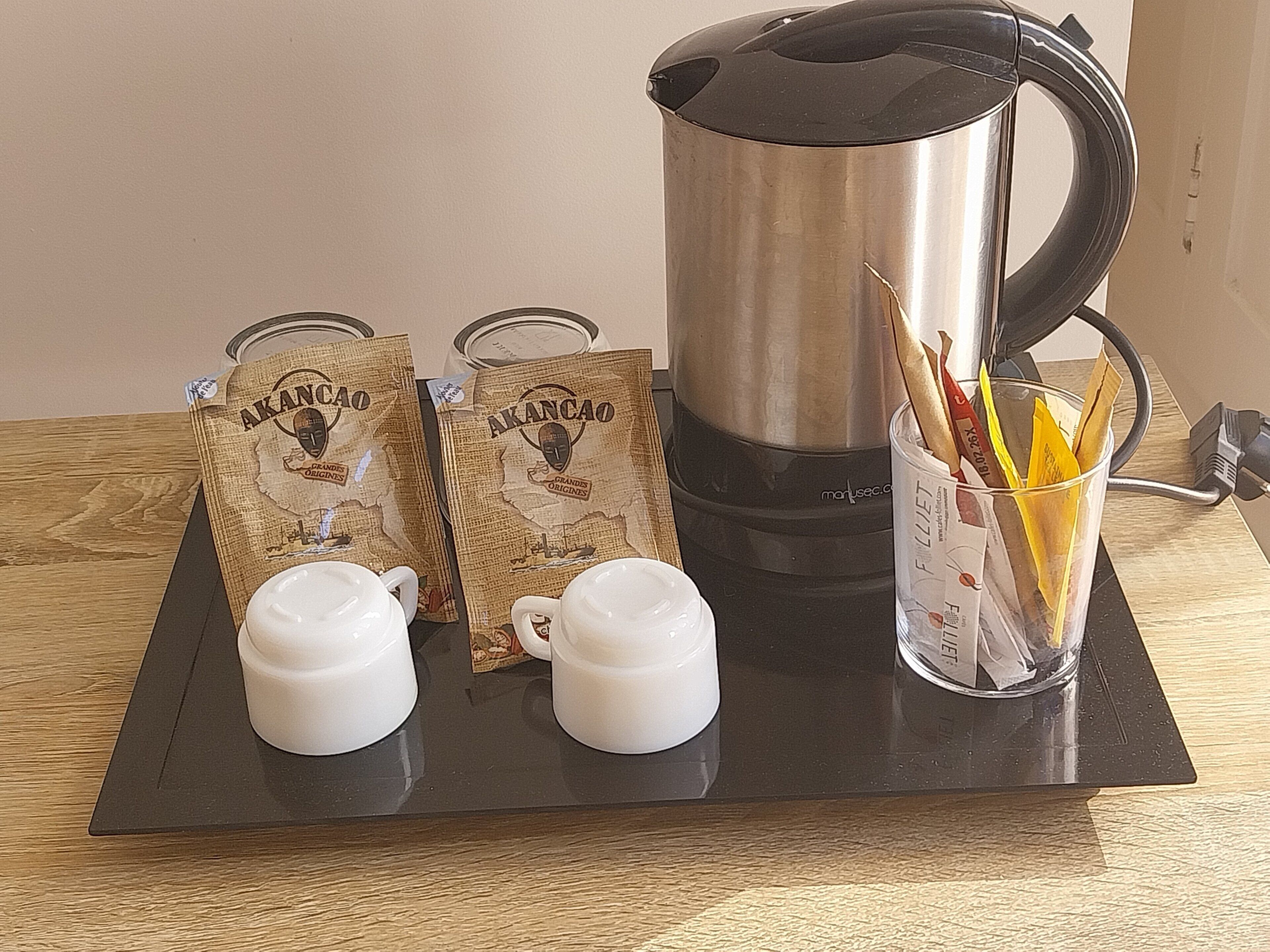 A tray with a coffee maker, two cups, two bags of Akancao coffee, and a glass with straws and coffee packets.