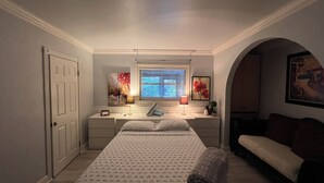 Un dormitorio con cama, mesitas de noche, escritorio, ventana con persianas, lámpara y un cuadro.