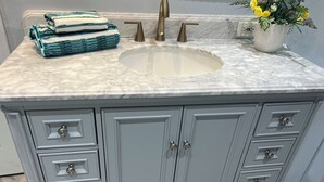 Un tocador de baño con encimera de mármol, un lavabo y una planta en maceta.