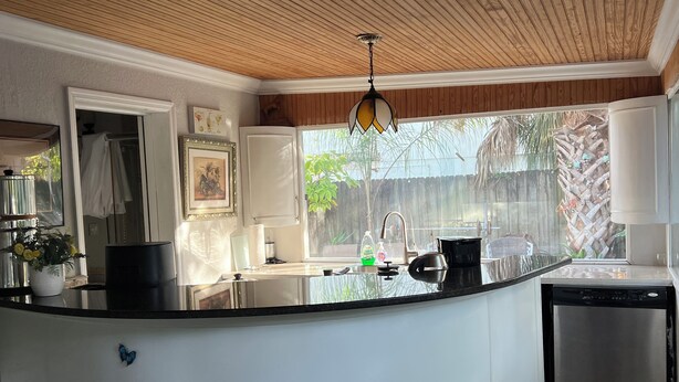 Una cocina con techo de madera, encimera negra, dos taburetes negros y lavavajillas.