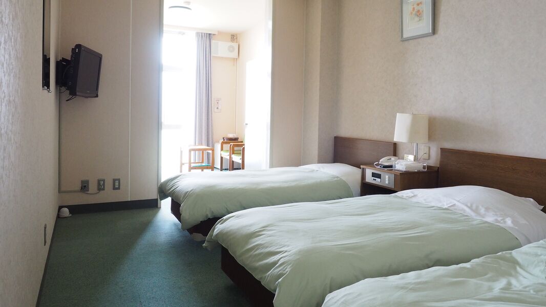 A hotel room with two beds, a desk with a lamp, a television mounted on the wall, and a view of the outside.