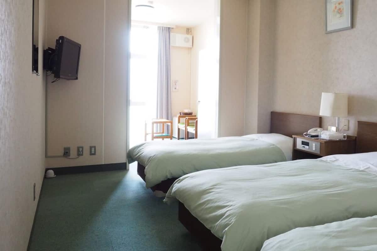 Habitación de hotel con dos camas, un escritorio con lámpara, un televisor en la pared y vistas al exterior.