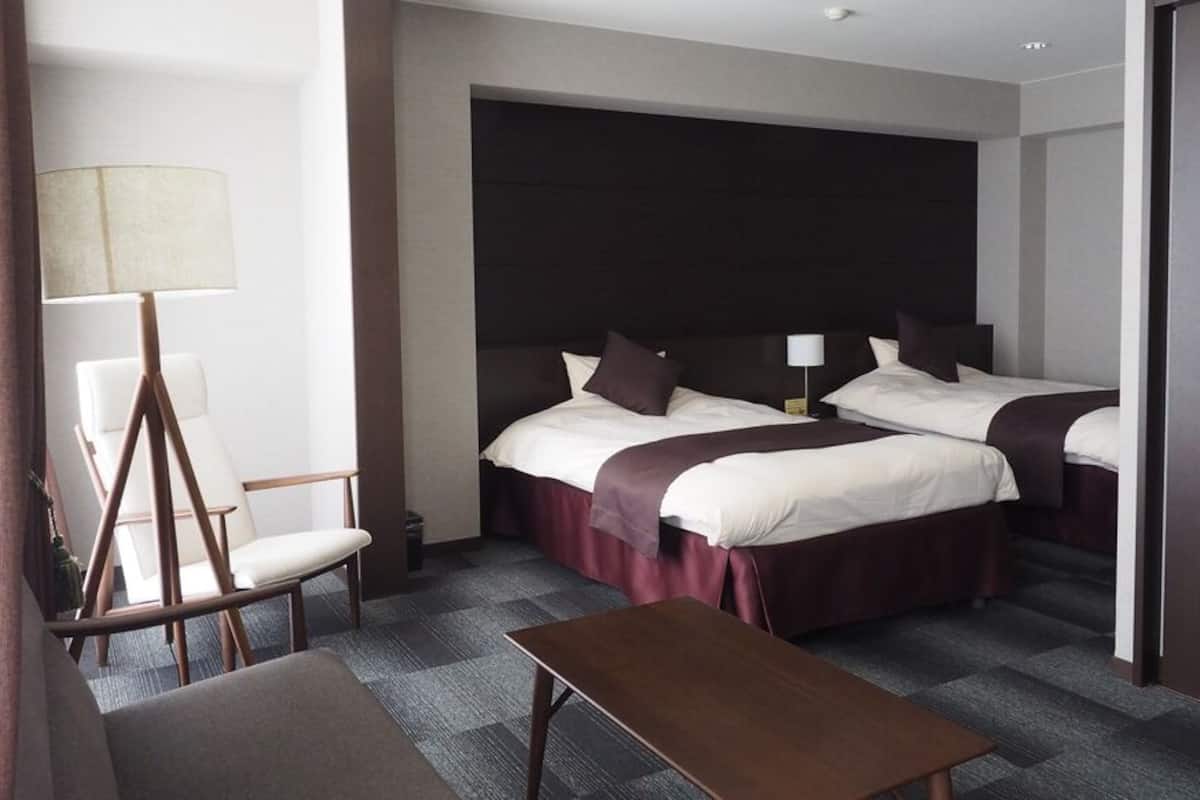 Una habitación de hotel con dos camas, un escritorio, una silla y una lámpara.