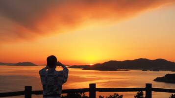 A person taking a photo of a sunset over a body of water with mountains in the background.