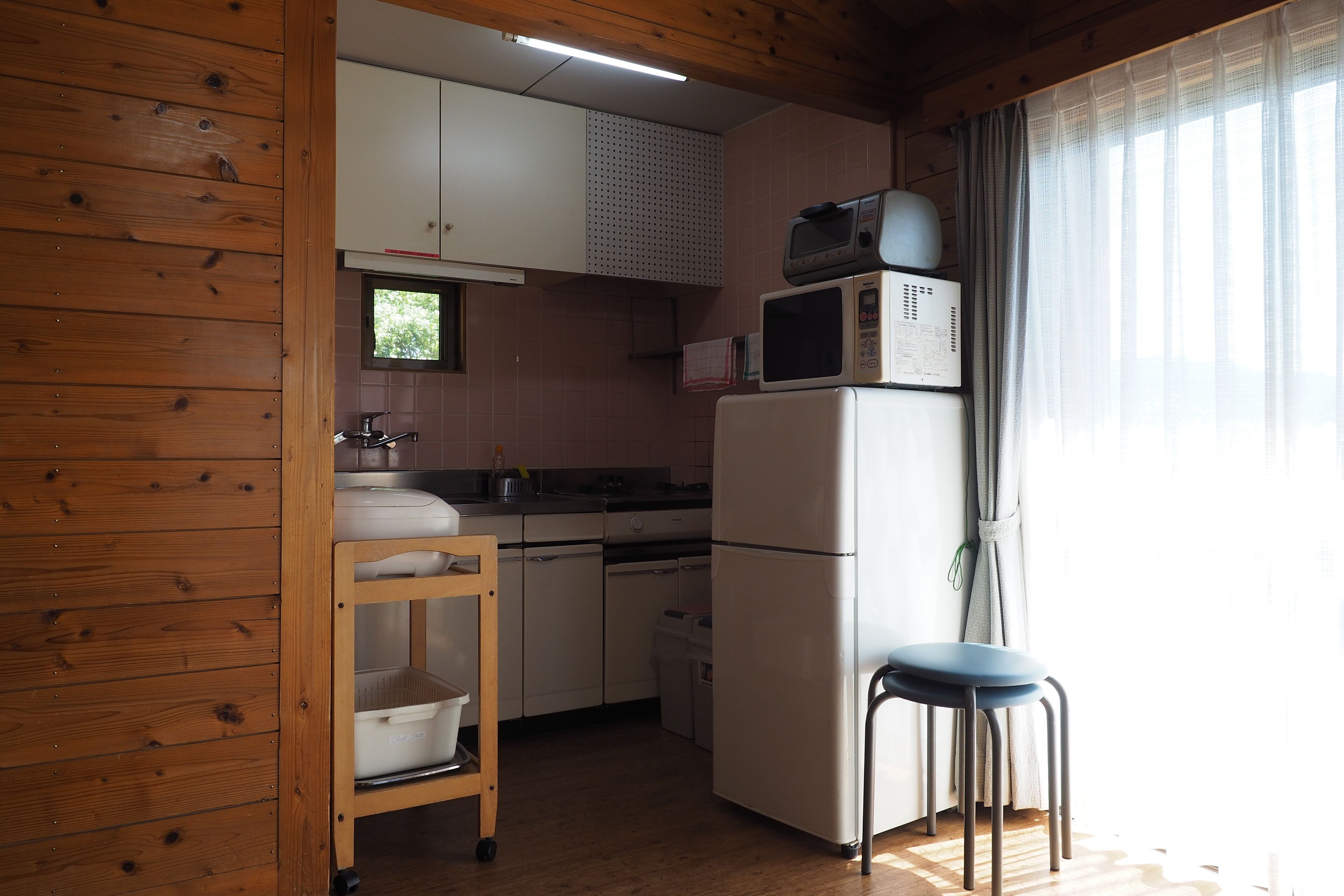A compact kitchen with wooden walls, white cabinets, a microwave, and a refrigerator.