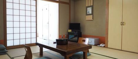 A traditional Japanese room with tatami flooring, a low table, a television, and sliding doors.