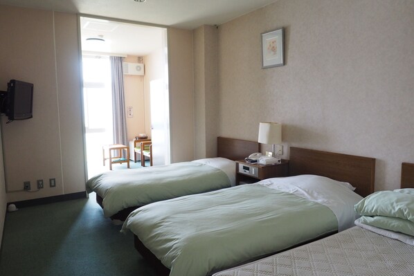 Habitación de hotel con dos camas, un escritorio con lámpara, televisor y puerta que da a un balcón.