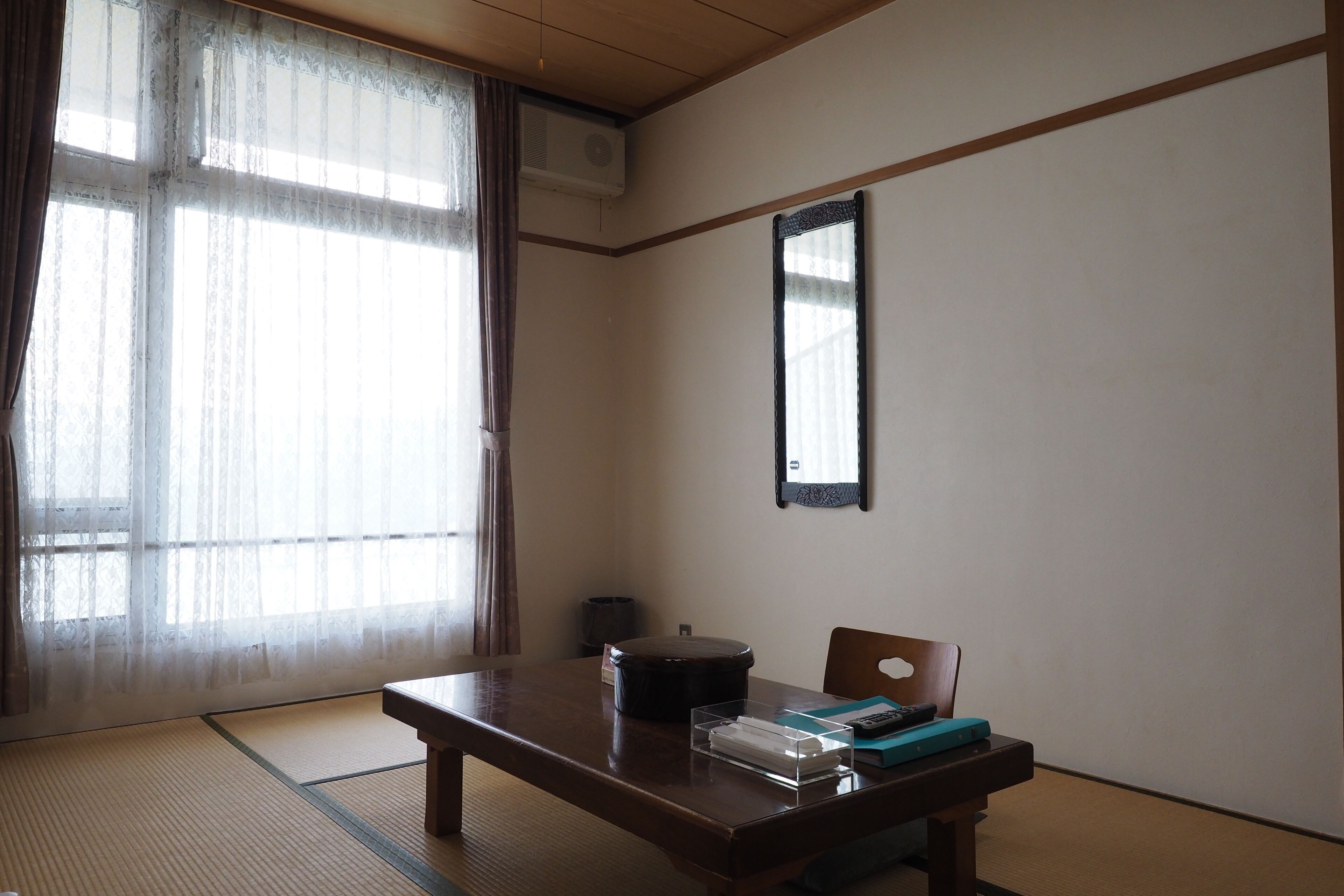 A traditional Japanese room with tatami flooring, a low wooden table, a black lacquered container, and a mirror on the wall.