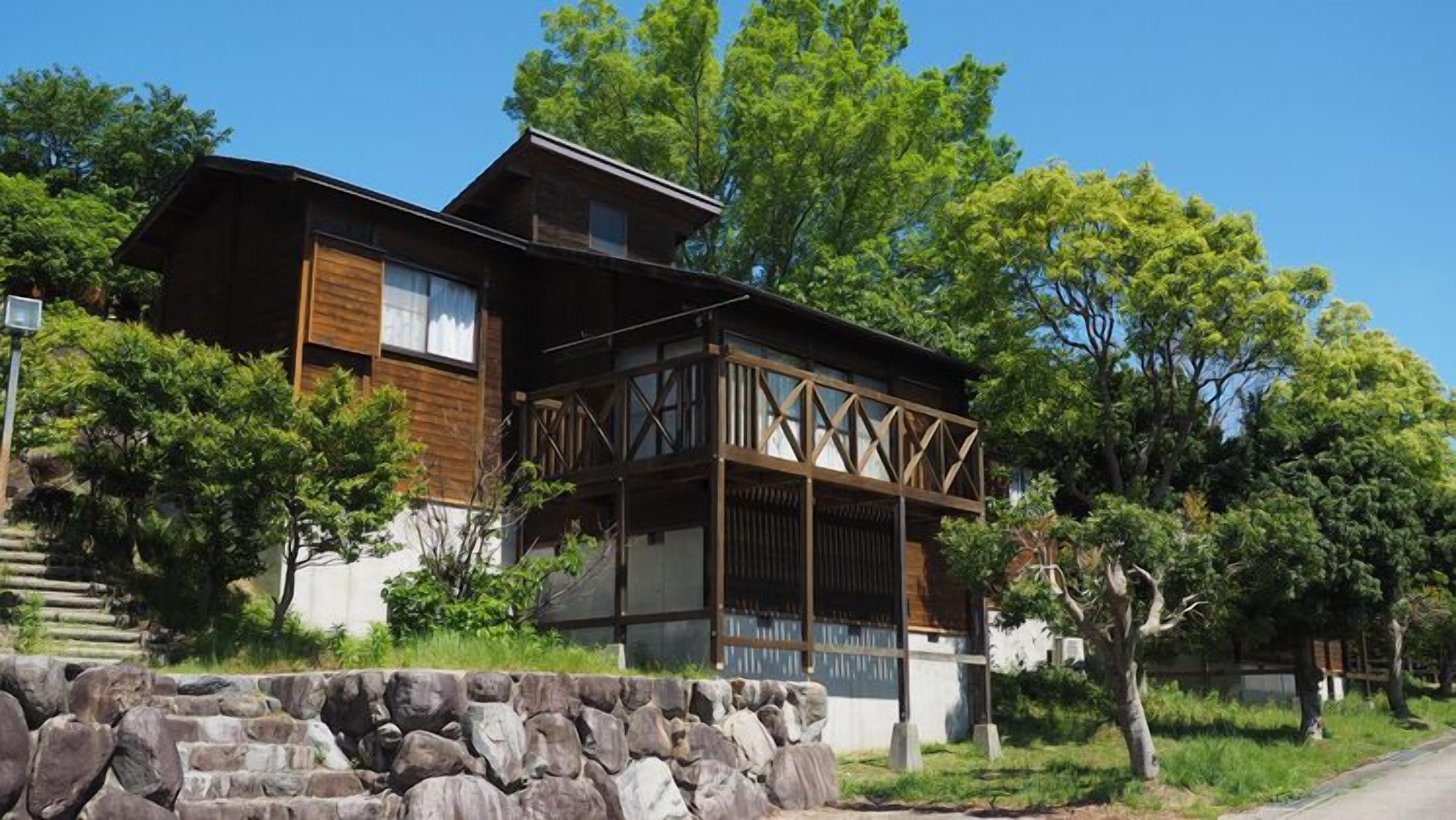 A two-story house with a wooden exterior, a balcony, and a stone wall in front.