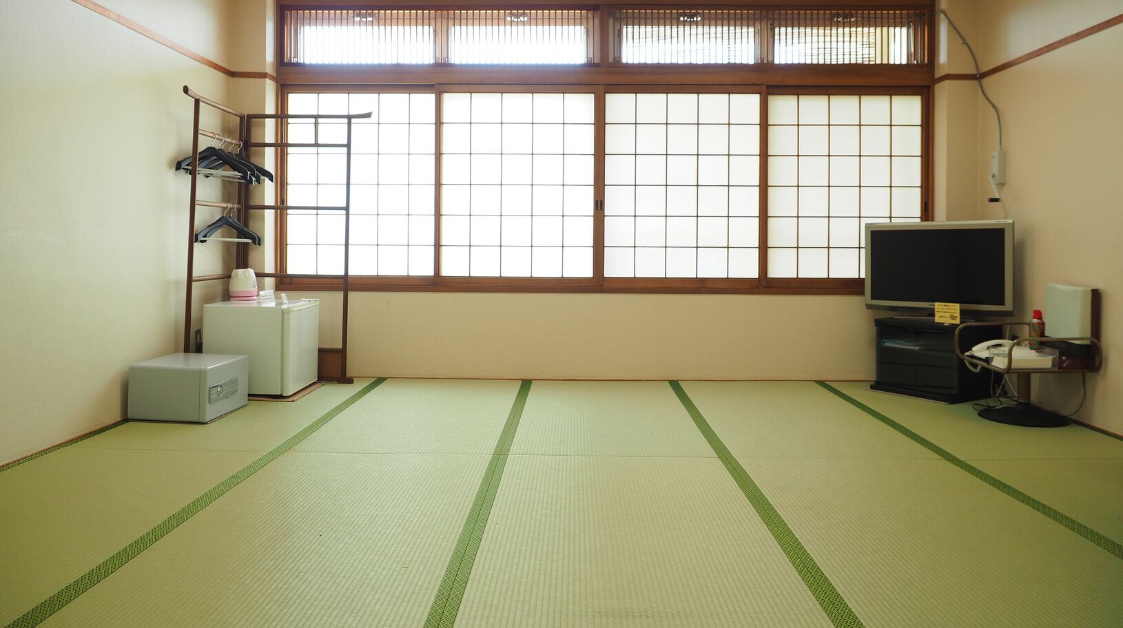 A room with tatami flooring, a television, a desk with a computer, and a window with traditional shoji screens.