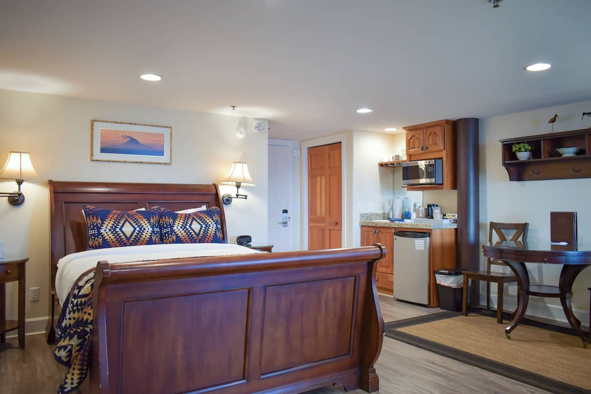 A hotel room with a wooden bed, a small kitchenette, and a dining area.