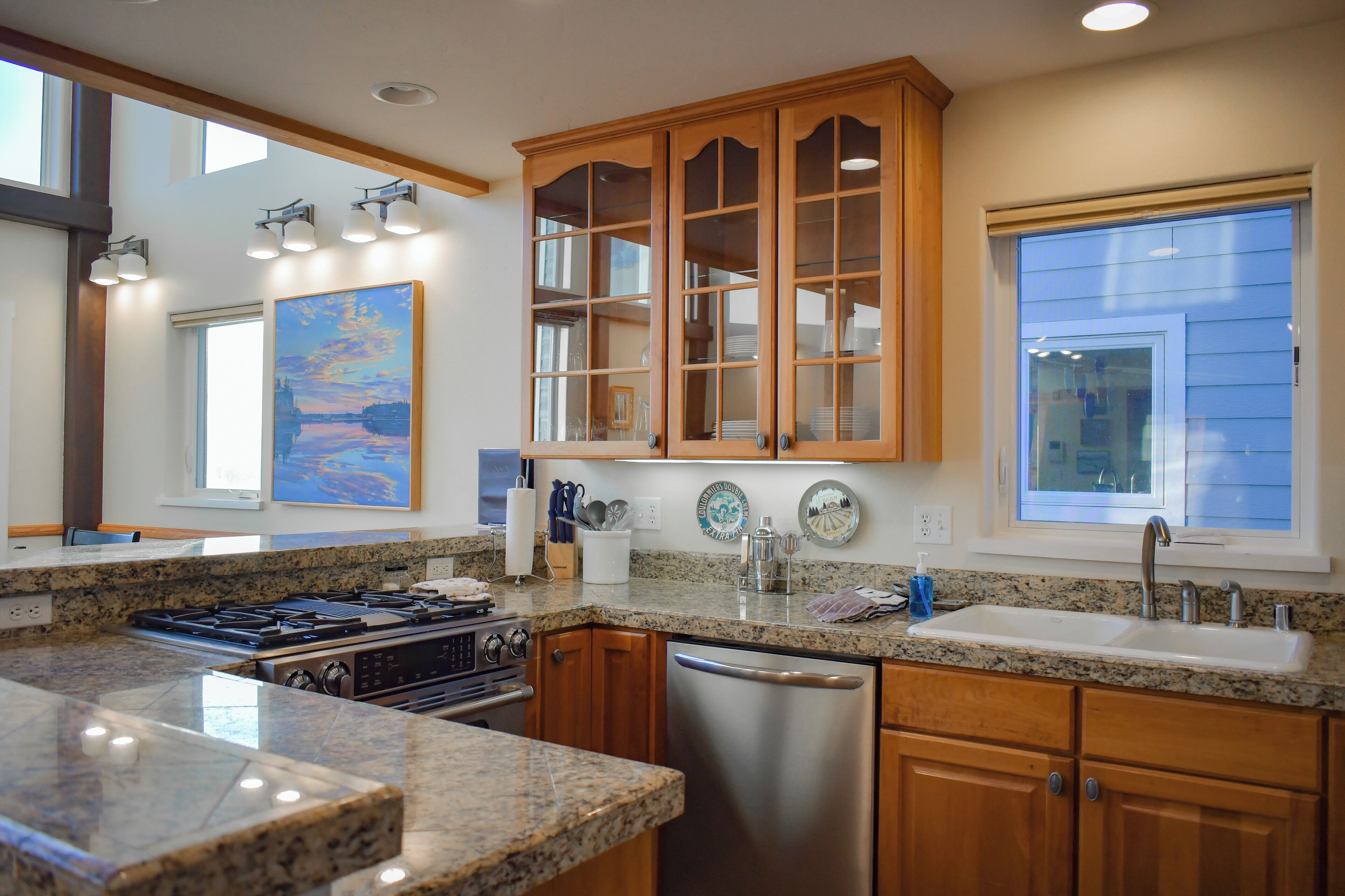 A modern kitchen with granite countertops, stainless steel appliances, wooden cabinets, and a large window providing natural light.