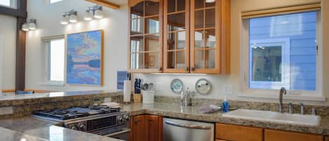 A modern kitchen with granite countertops, stainless steel appliances, wooden cabinets, and a large window providing natural light.