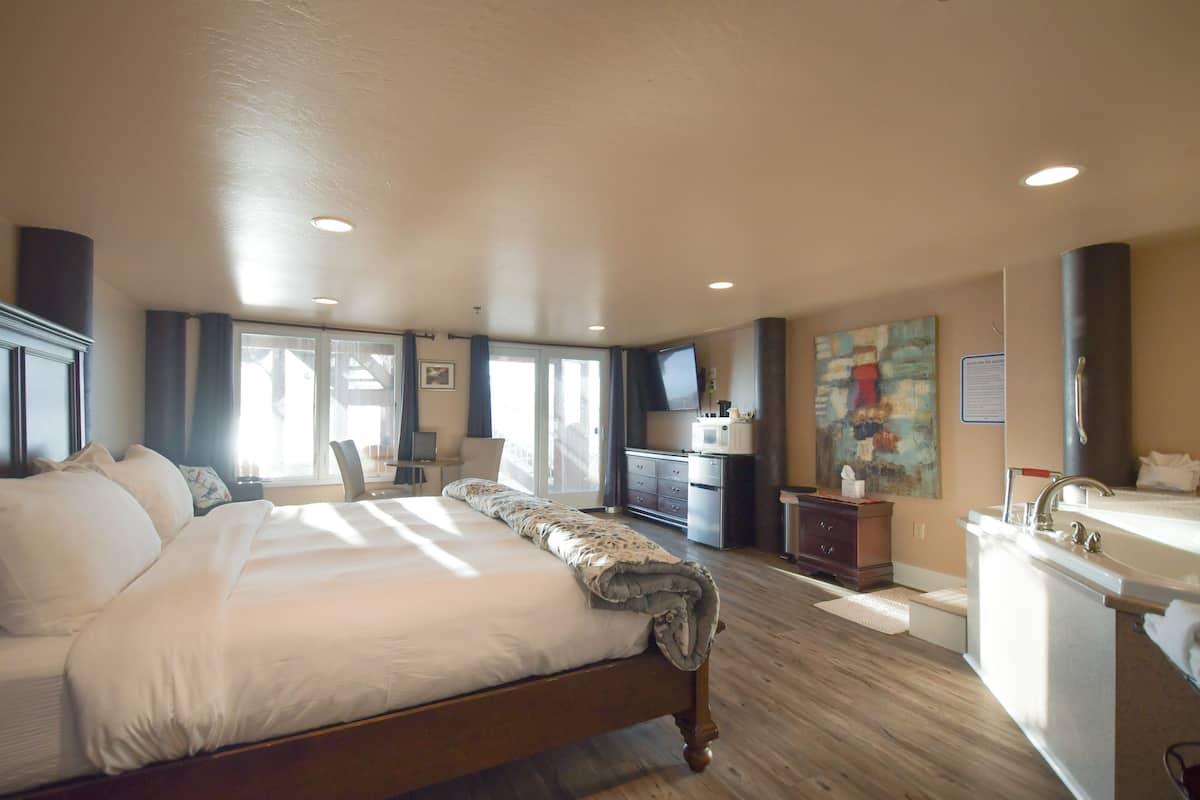 A spacious bedroom with a large bed, a desk, and a bathroom with a sink and mirror.
