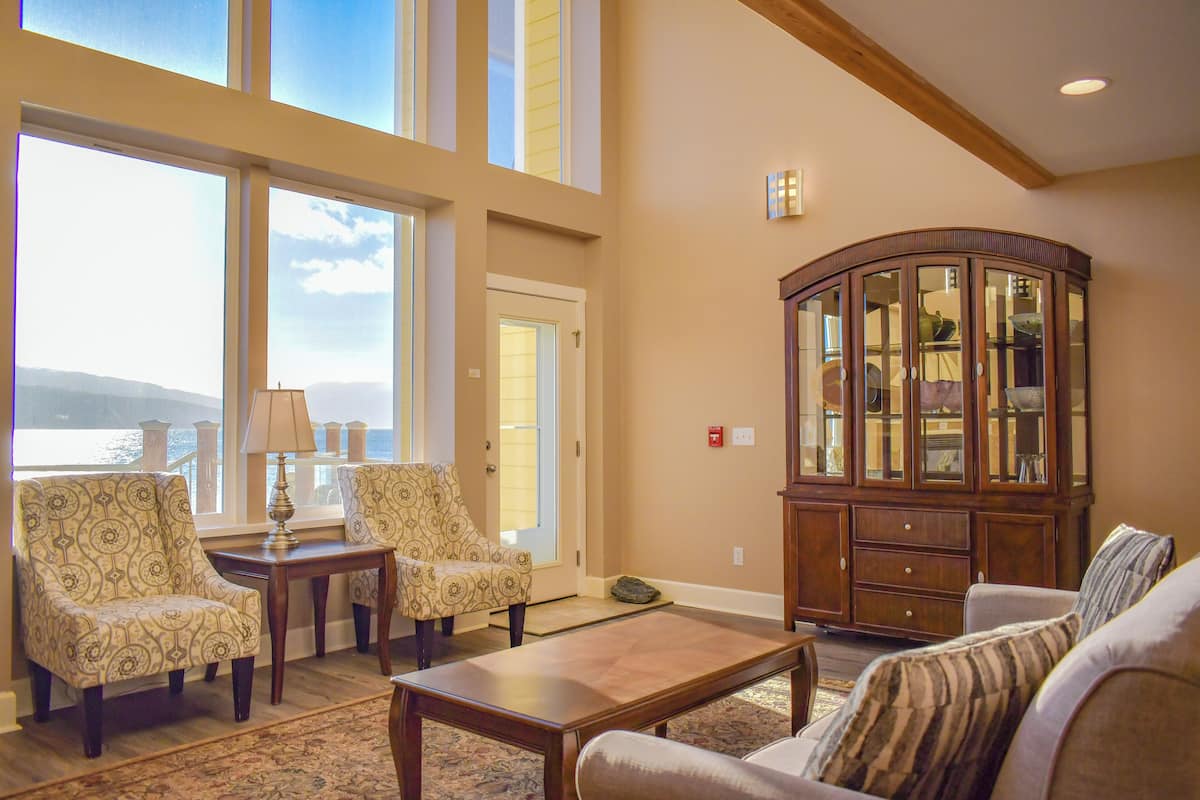 A spacious living room with large windows, a wooden cabinet, and patterned chairs.