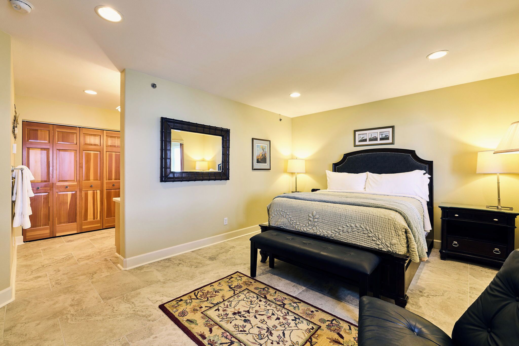 A bedroom with a bed, bedside tables, a bench, a mirror, and a door to a bathroom.